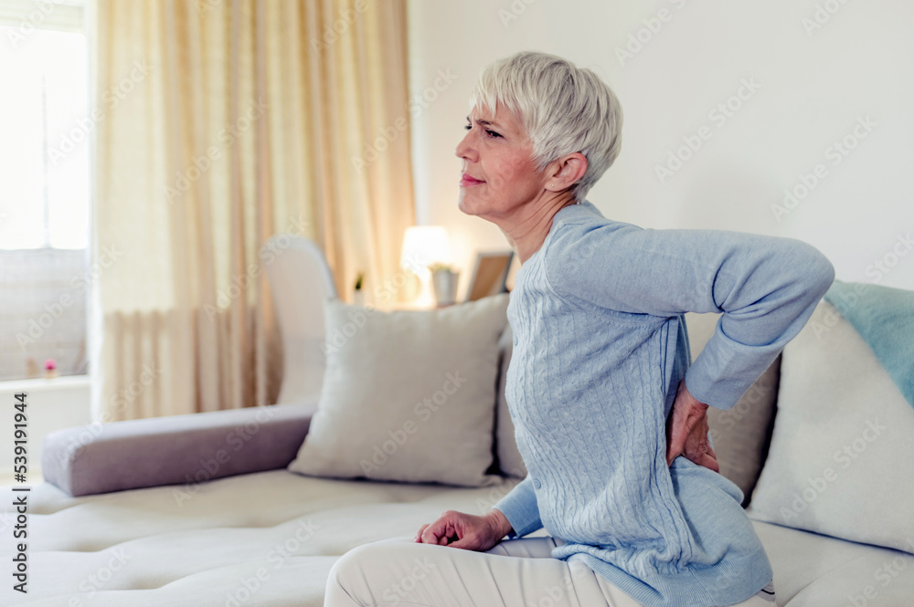Woman feels back pain, massaging aching muscles. Mature woman feeling morning discomfort in aching back in the living room. Woman feels back pain, massaging aching muscles. Mature woman feeling morning discomfort in aching back in the living room.