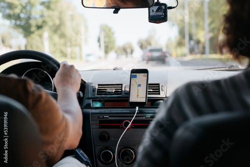 Фототапет Rear view of a couple of people driving a car using a map navigator mobile app