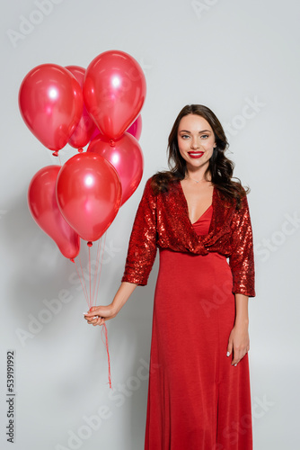 Young woman in red dress holding festive balloons on grey background © LIGHTFIELD STUDIOS