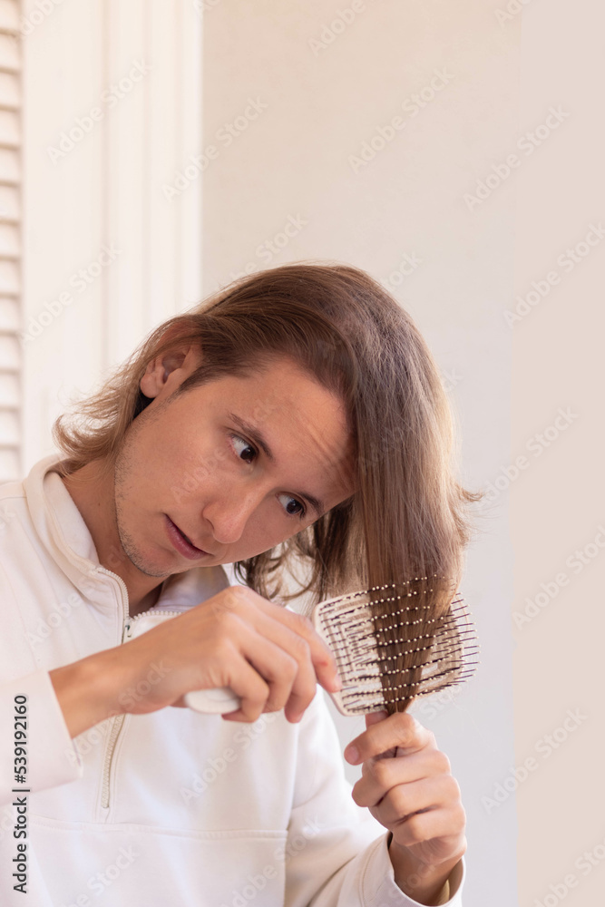 Vertical view of young long haired man taking care and brushing his hair with anti fall hair brush in white background Vertical view of young long haired man taking care and brushing his hair with anti fall hair brush in white background