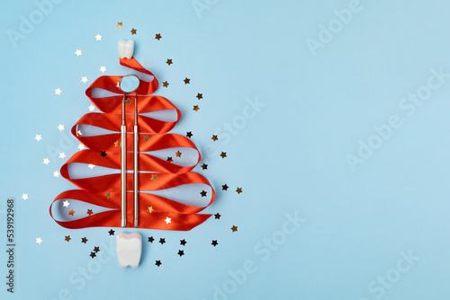 mirror, probe, dental kid instruments on red ribbon for new year on fir with teeth. tooth in santa hat on snow. Creative medical christmas winter background. Health care, hygiene concept. Copy space