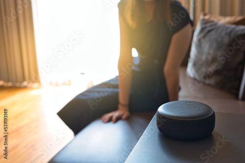 Woman sitting on a chair and talking to a speech recognition device, Amazon Alexa with sunlight background