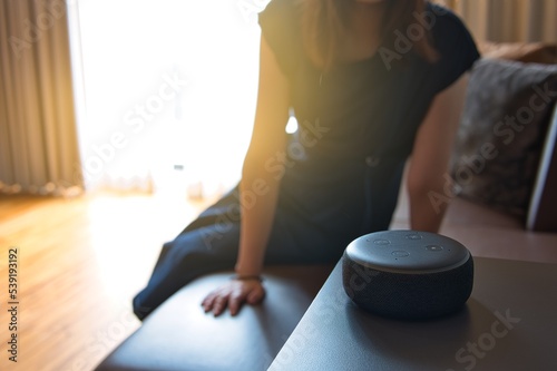 Woman sitting on a chair and talking to a speech recognition device, Amazon Alexa with sunlight background