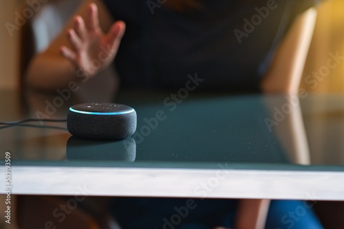 Woman sitting on a chair and talking to a speech recognition device, Amazon Alexa with sunlight background