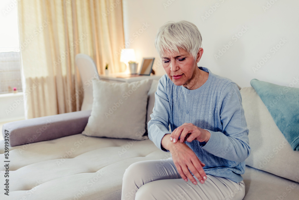 Photo of painful wrist in an elderly person. Senior woman suffering from pain in wrist at home while sitting on a gray sofa. Mature woman feeling wrist pain, injury problem, healthcare concept, sprain Photo of painful wrist in an elderly person. Senior woman suffering from pain in wrist at home while sitting on a gray sofa. Mature woman feeling wrist pain, injury problem, healthcare concept, sprain