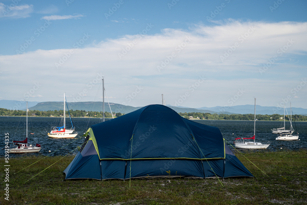 Tent set up on a campground near a bay with anchored sailboats at lake Champlain