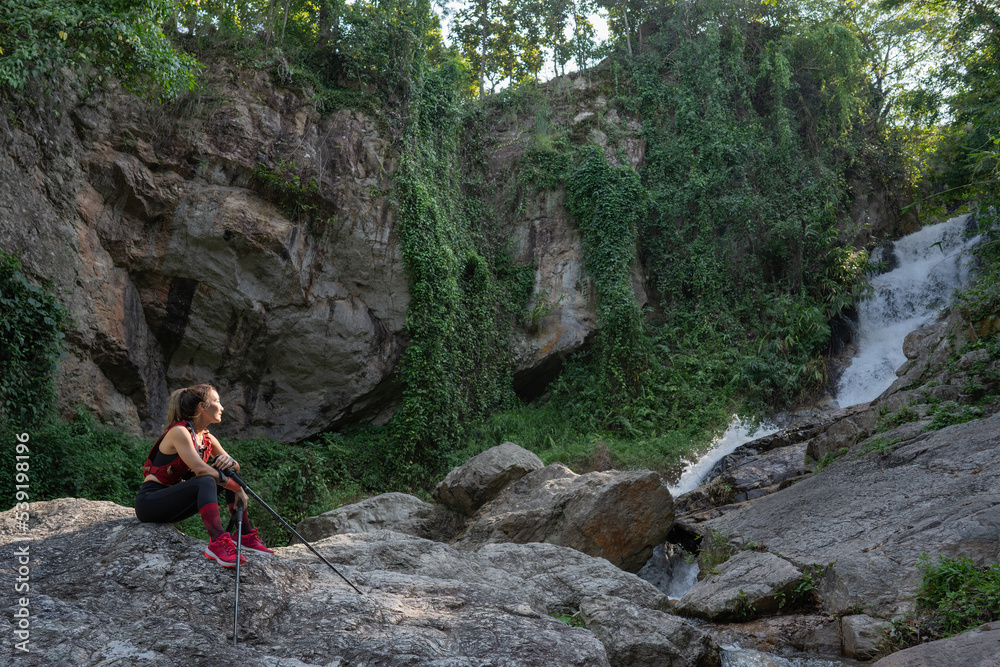 Athletic woman resting after running in the mountain and looking at to waterfall