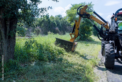 Municipal worker driving using mechanical mower mowing grass on roadside suburban highway road maintenance service photo