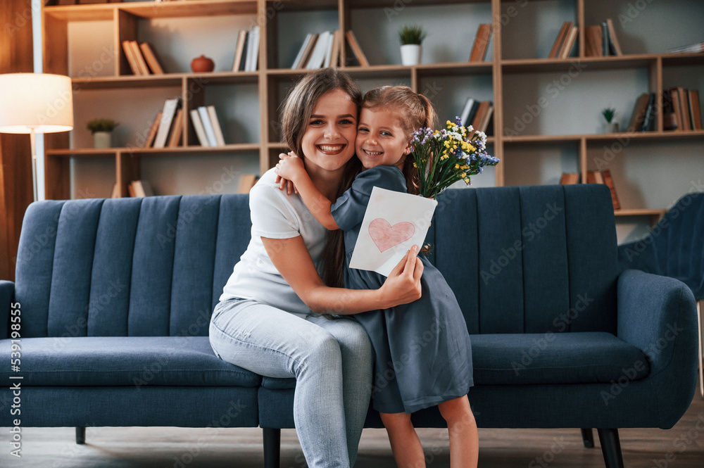 Embracing each other. Giving the gift. Young mother with her daughter is together at apartment Embracing each other. Giving the gift. Young mother with her daughter is together at apartment