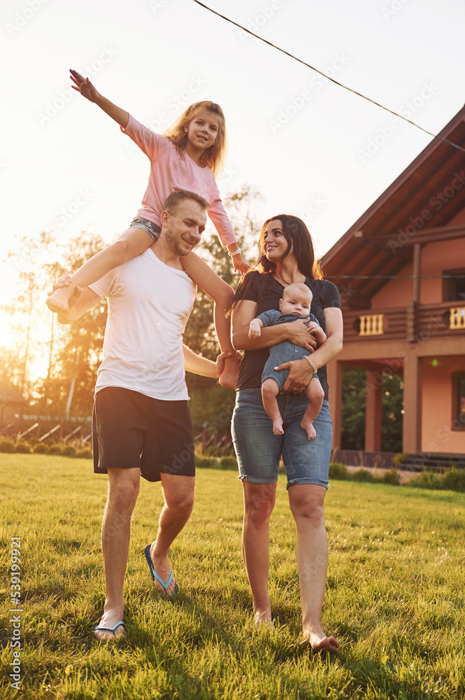 Obraz premium Girl is on the shoulders of man. Father and mother with daughter and little son is outdoors on the field