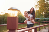 Woman is on the man's back. Happy wife and husband is outdoors on the wooden bridge at sunny day