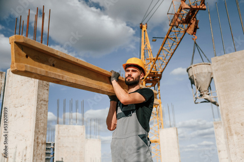 Front view of man that is in uniform holding wooden plank on the construction site