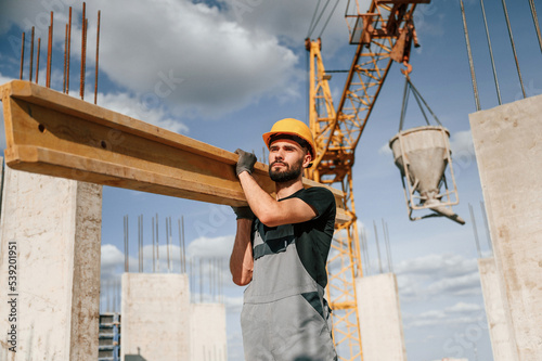 Front view of man that is in uniform holding wooden plank on the construction site