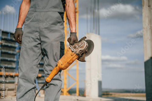 Holding grinding machine. Man in uniform is working on the construction site