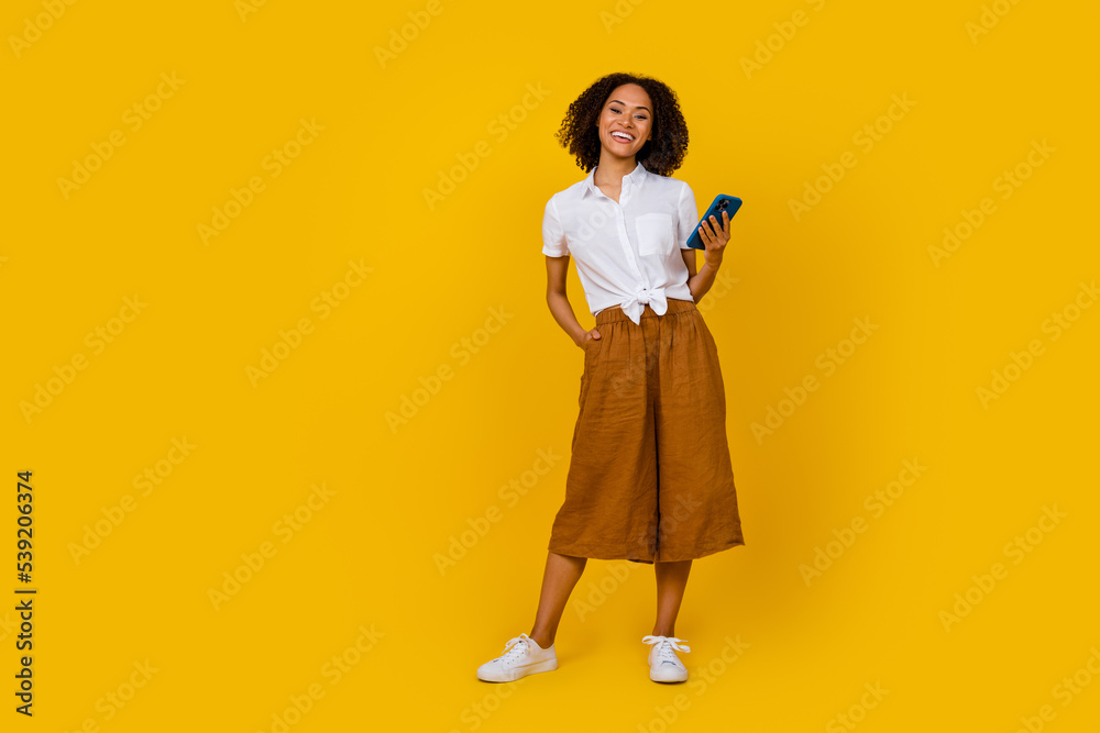 Full body portrait of pretty cheerful person hold telephone have good mood isolated on yellow color background Full body portrait of pretty cheerful person hold telephone have good mood isolated on yellow color background