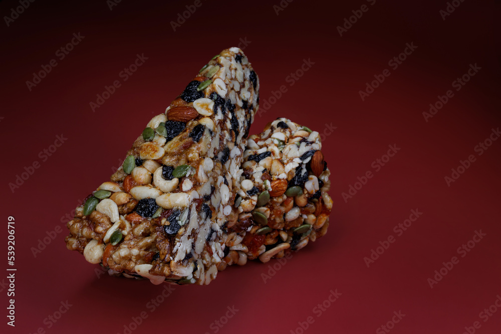 Two pieces of gozinak from various nuts with dried fruits on a red background. Two pieces of gozinak from various nuts with dried fruits on a red background.