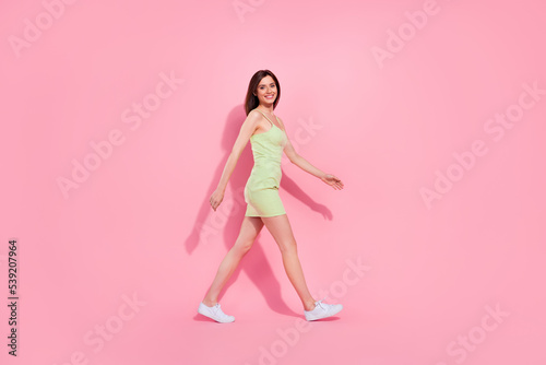 Full length photo of cute adorable young girl dressed green outfit smiling walking isolated pink color background