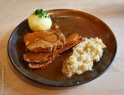Auf einem Teller liegen ein Kartoffelkloß, Schweinebratenscheiben und Sauerkraut.