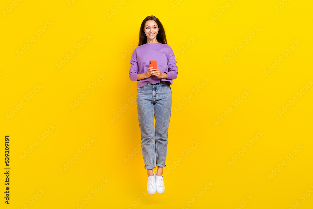Full length photo of positive cheerful lady wear violet trendy clothes rejoice bun new modern gadget device telephone isolated on yellow color background Full length photo of positive cheerful lady wear violet trendy clothes rejoice bun new modern gadget device telephone isolated on yellow color background