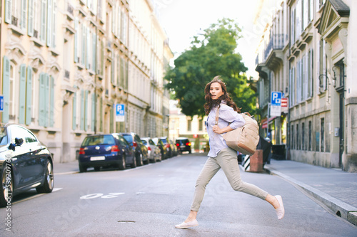 Outdoor portrait of beautiful young woman walking down the street, wearing backpack, city background