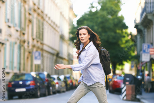 Outdoor portrait of beautiful young woman walking down the street, wearing backpack, city background © annanahabed