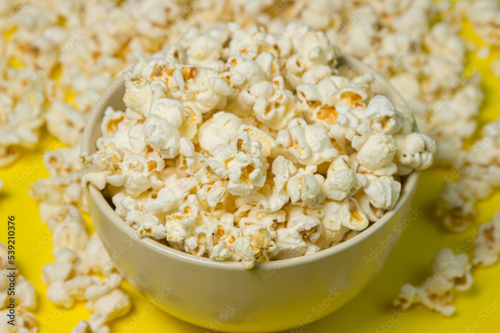 A plate full of popcorn on a yellow background. Delicious salty popcorn