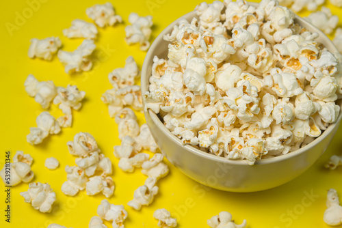 A plate full of popcorn on a yellow background. Delicious salty popcorn