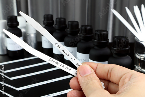 blotter papers are in a right hand with background essential oil and frangrance oil bottle for testing smell during blending process for choosing nice scent for scented candles and body perfume in lab