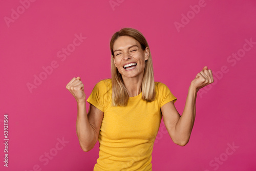 Cheerful adult european lady rejoices to victory and makes success gesture with hands
