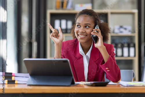 Young businesswoman cheerful african american lady working at workplace office, workdesk with laptop financial documents having phone conversation, copy space