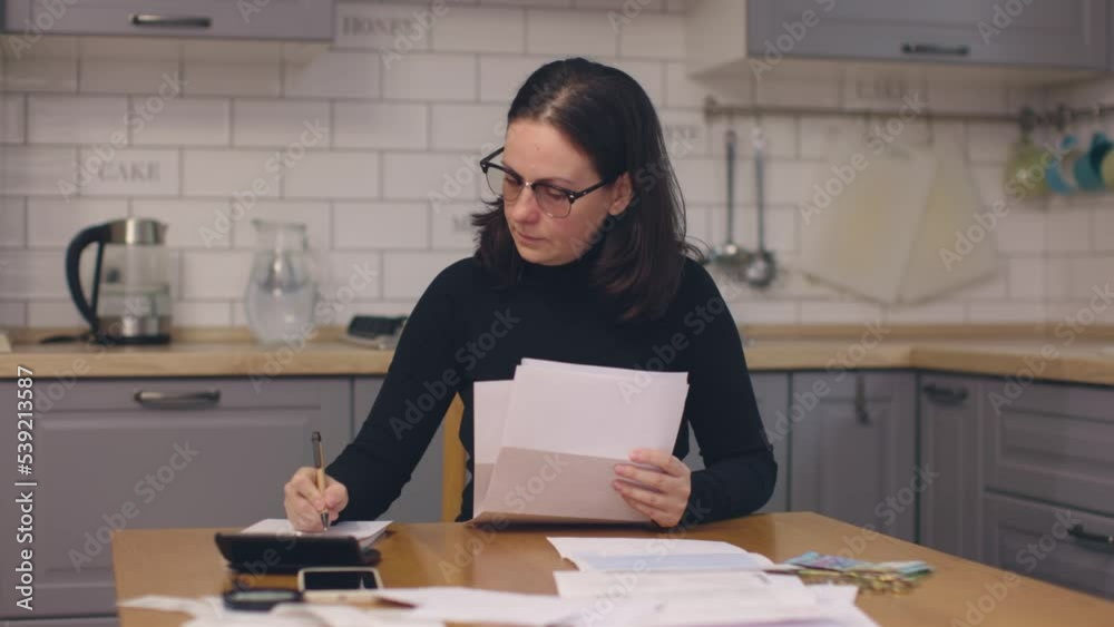 female in black sit kitchen table look through paper documents sorting papers planning expenses family money budget. calculating write down numbers using pen notepad. utility bills bank invoices 