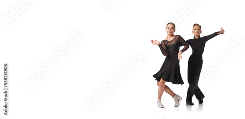 фотографія Two kids, school age girl and boy in black stage costumes dancing ballroom dance isolated on white background