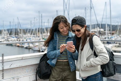 two happy asian korean female travelers looking at recommended restaurants online on the phone while discussing their lunch plan Old Fishermanâs Wharf in California. © PR Image Factory