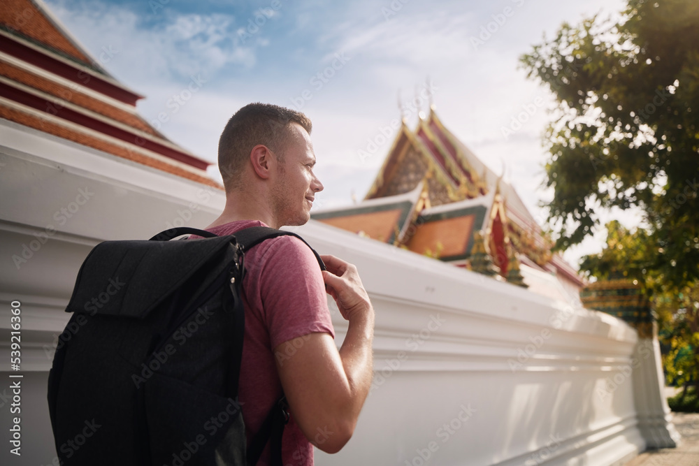 Tourist with backpack walking on street against Buddhist temple. Bangkok, Thailand..