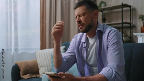 Serious sad young man use phone sitting on sofa at home. Communication businessman chatting scrolling social media. Close up. Portrait. Slow motion