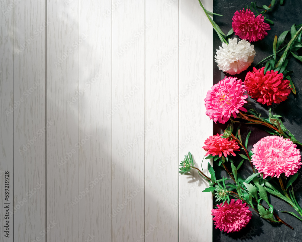 Naklejka premium Chaotically scattered aster flowers are on a dark rough background next to an empty white wooden table. Abstract floral autumn composition with copy space.