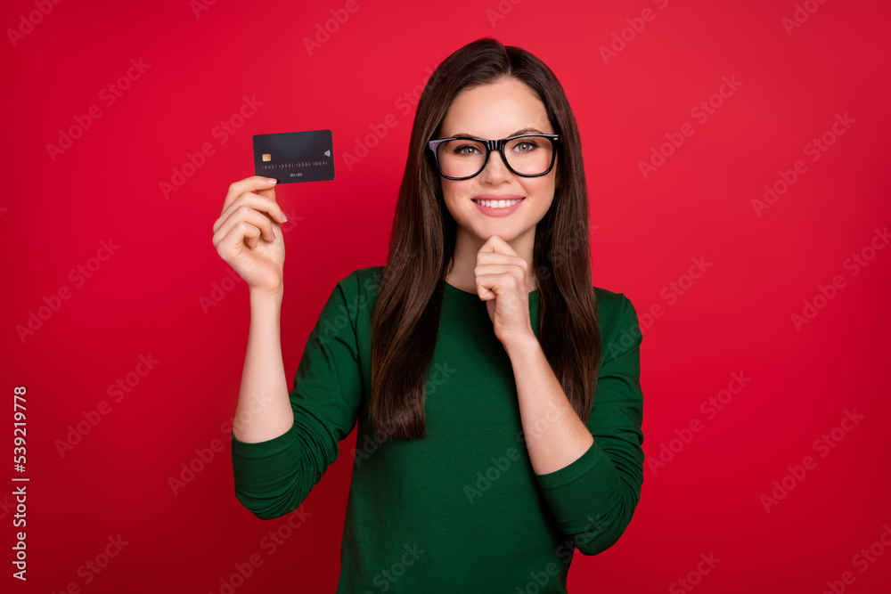Photo of attractive woman bank client card user hand touch chin dressed stylish green outfit specs isolated on shine red color background Photo of attractive woman bank client card user hand touch chin dressed stylish green outfit specs isolated on shine red color background