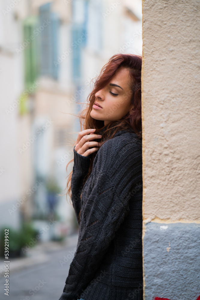 Woman standing against a wall in an empty street looking sad
