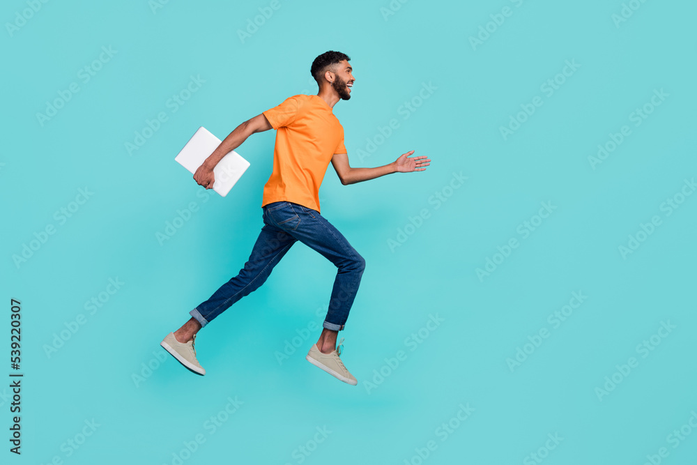 Full length profile photo of crazy guy jump hurry rush empty space hold laptop isolated on teal color background Full length profile photo of crazy guy jump hurry rush empty space hold laptop isolated on teal color background