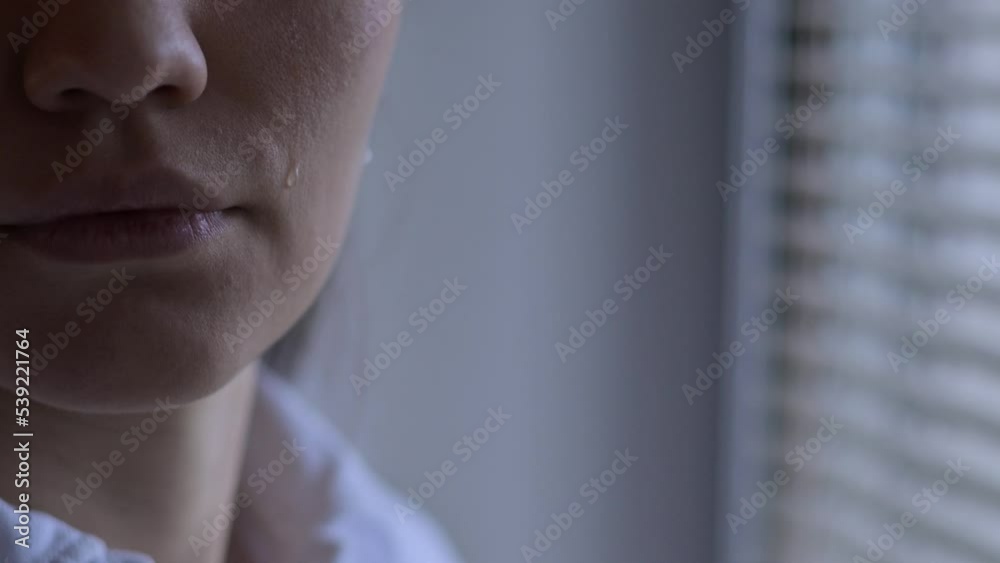 Close-up of a tear that rolls down the cheek of a woman who is standing near the window. The emotion of experiencing what is happening in the world - wars, disasters, epidemics and catastrophes