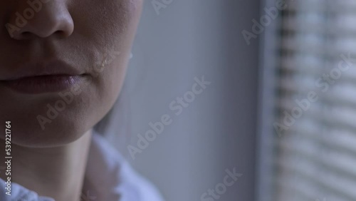 Close-up of a tear that rolls down the cheek of a woman who is standing near the window. The emotion of experiencing what is happening in the world - wars, disasters, epidemics and catastrophes