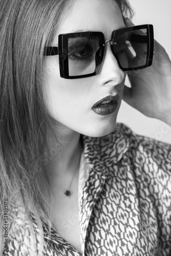 Fashion and style concept. Close-up retro woman portrait with big sunglasses and make-up. Model holding hand near glasses. Selective focus. Eyes is in camera focus. Black and white image
