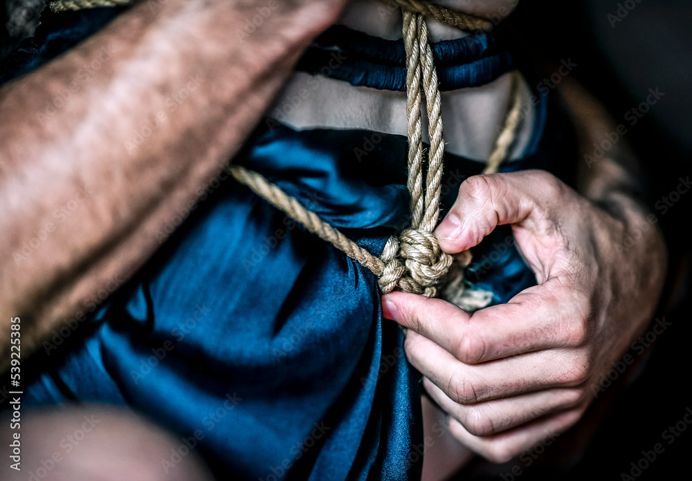 A young, slim, naked hot woman with knots of natural ropes held by her boyfriend. Ancient Japanese art of aesthetic bondage and tying shibari kinbaku. Concept of BDSM sex games.