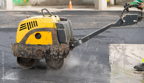 a worker operates a yellow machine to crush the tar
