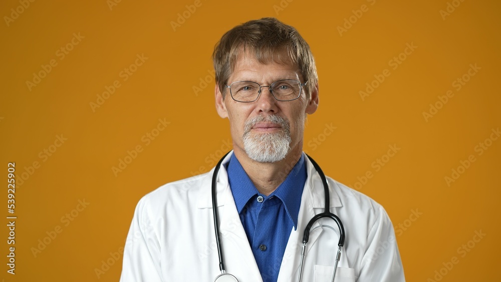 Portrait of tired handsome doctor man in professional medical white coat is isolated on solid yellow studio background. Bored doctor with beard and stethoscope Portrait of tired handsome doctor man in professional medical white coat is isolated on solid yellow studio background. Bored doctor with beard and stethoscope