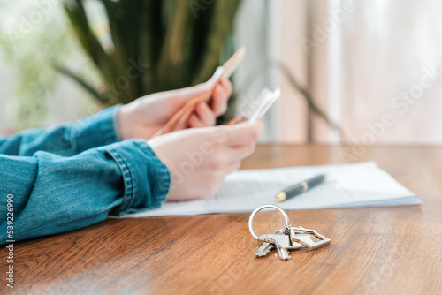 Close up of key with keychain lies on the table. Defocused female's hands counting money at the background. Concept of purchase of real estate, leasing and mortgage photo