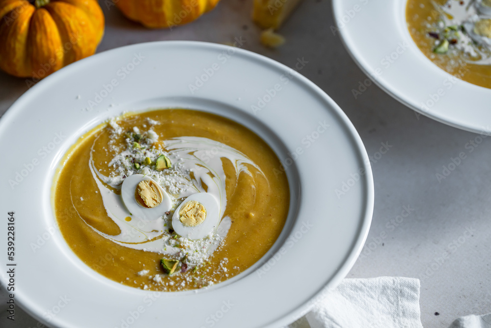 Homemade pumpkin cream soup with quail eggs, parmesan , sour cream and pistachios on white background Homemade pumpkin cream soup with quail eggs, parmesan , sour cream and pistachios on white background