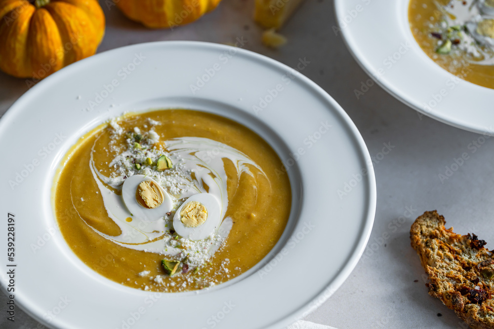 Homemade pumpkin cream soup with quail eggs, parmesan , sour cream and pistachios and biscotti with dried tomatoes and pistachios on white background Homemade pumpkin cream soup with quail eggs, parmesan , sour cream and pistachios and biscotti with dried tomatoes and pistachios on white background