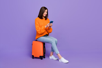 Full body photo of nice young lady typing chatting hold gadget travel wear trendy orange knitwear look isolated on violet color background