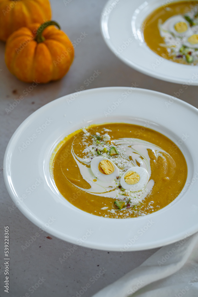 Homemade pumpkin cream soup with quail eggs, parmesan , sour cream and pistachios on white background Homemade pumpkin cream soup with quail eggs, parmesan , sour cream and pistachios on white background